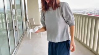 Alexandra Daddario wearing a grey sweatshirt with no bra and hard nipples as she helps her friend clean her feet on a balcony and then stands behind another friend waving her arms around and flapping them in the background as she talks with them