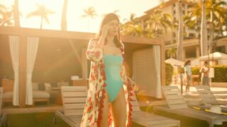 Alexandra Daddario talking on a phone while wearing a blue one-piece swimsuit, showing cleavage that bounces a bit as she shifts her weight from one foot to the other