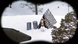 Vanessa Angel wearing a see-through white bra that shows her nipples underneath as she steps out a tent in a pair of panties, stretching her arms and then starting to zip into a snow suit as a guy watches through a pair of binoculars